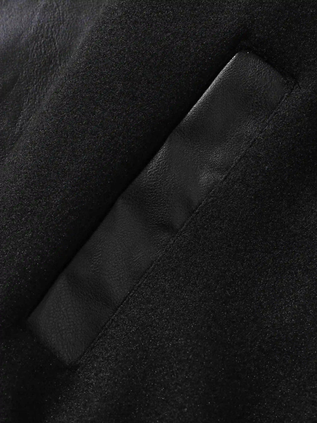 A tight crop highlighting the pocket detail on a black baseball jacket by TALISHKO.