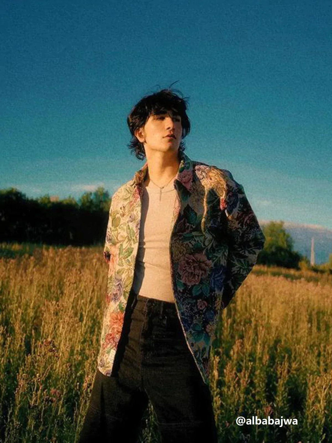 Person wearing a floral embroidered long-sleeved shirt by TALISHKO, standing in a sunlit field.