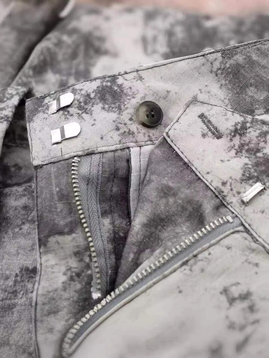A detailed view of TALISHKO's gray printed cargo pants, highlighting the zipper and button details.