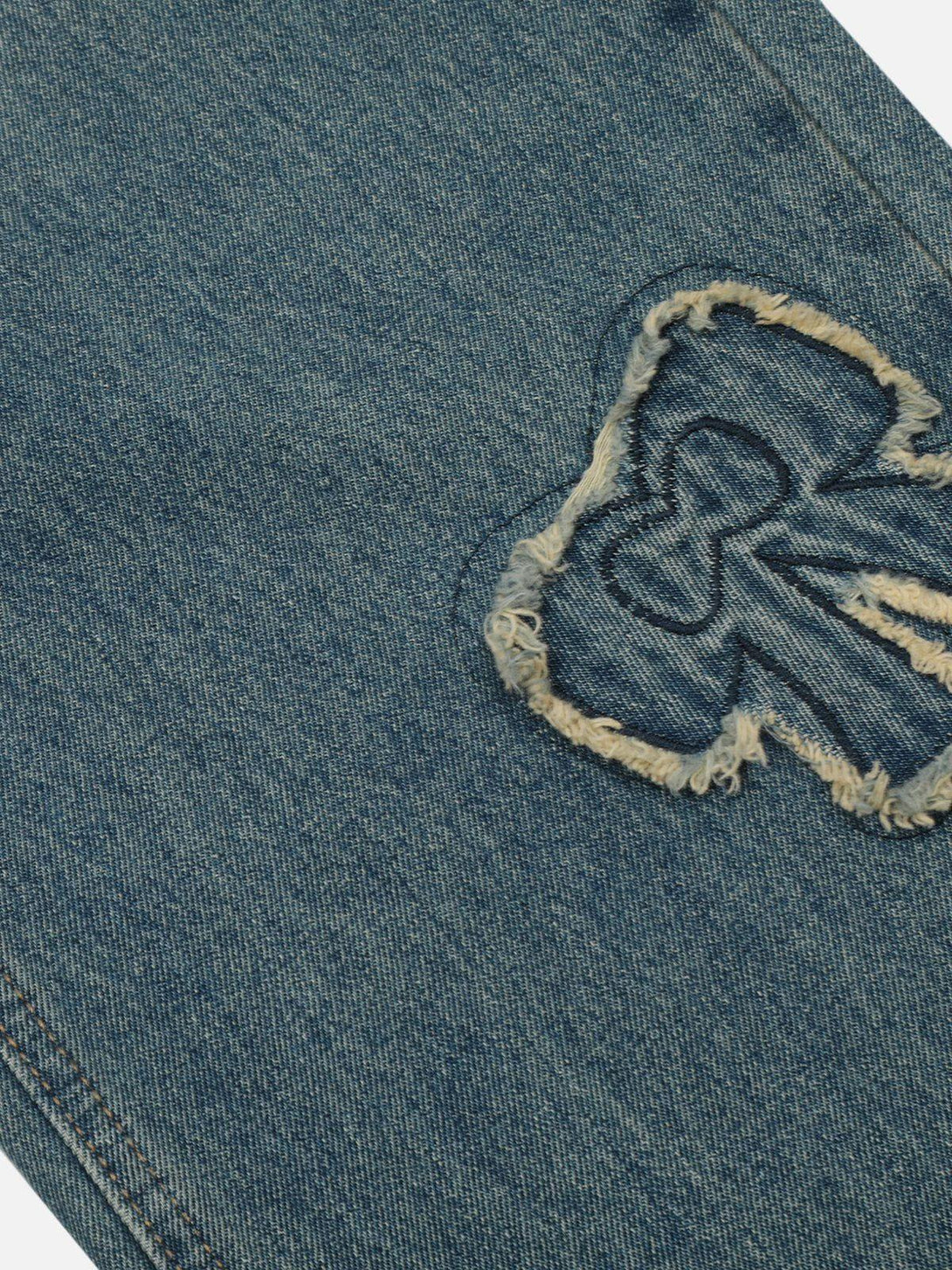A detailed view of TALISHKO fringe bow jeans, highlighting the textured fabric and stitching.