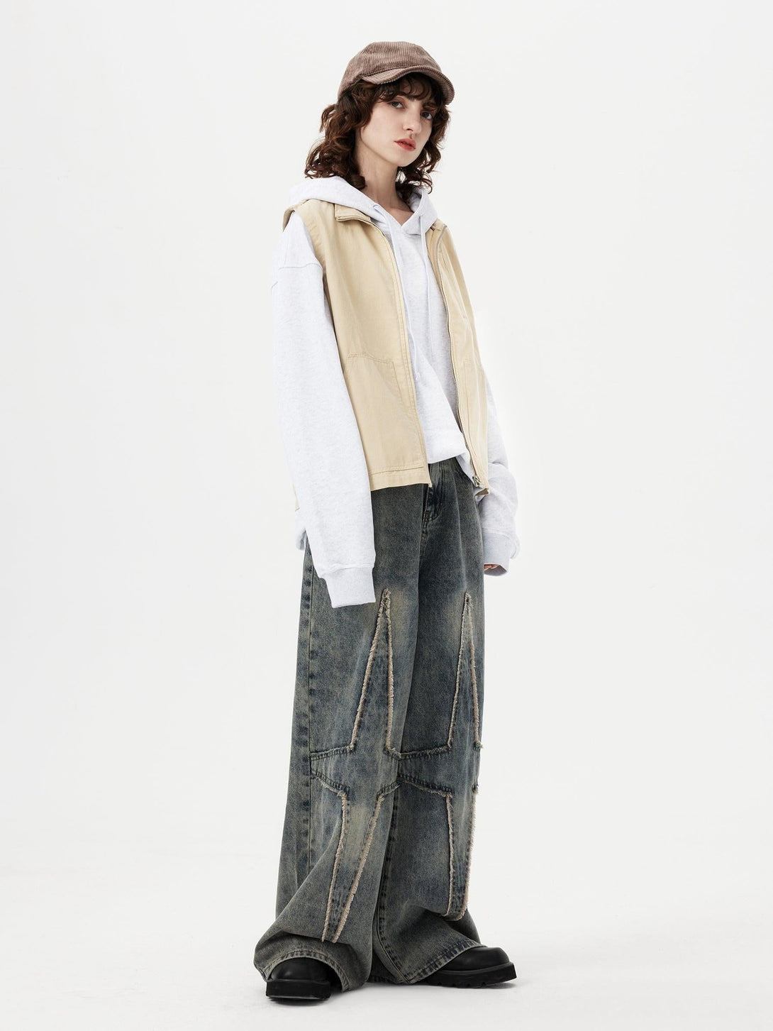Model wearing TALISHKO oversized fringe star jeans with a casual hoodie and vest ensemble.