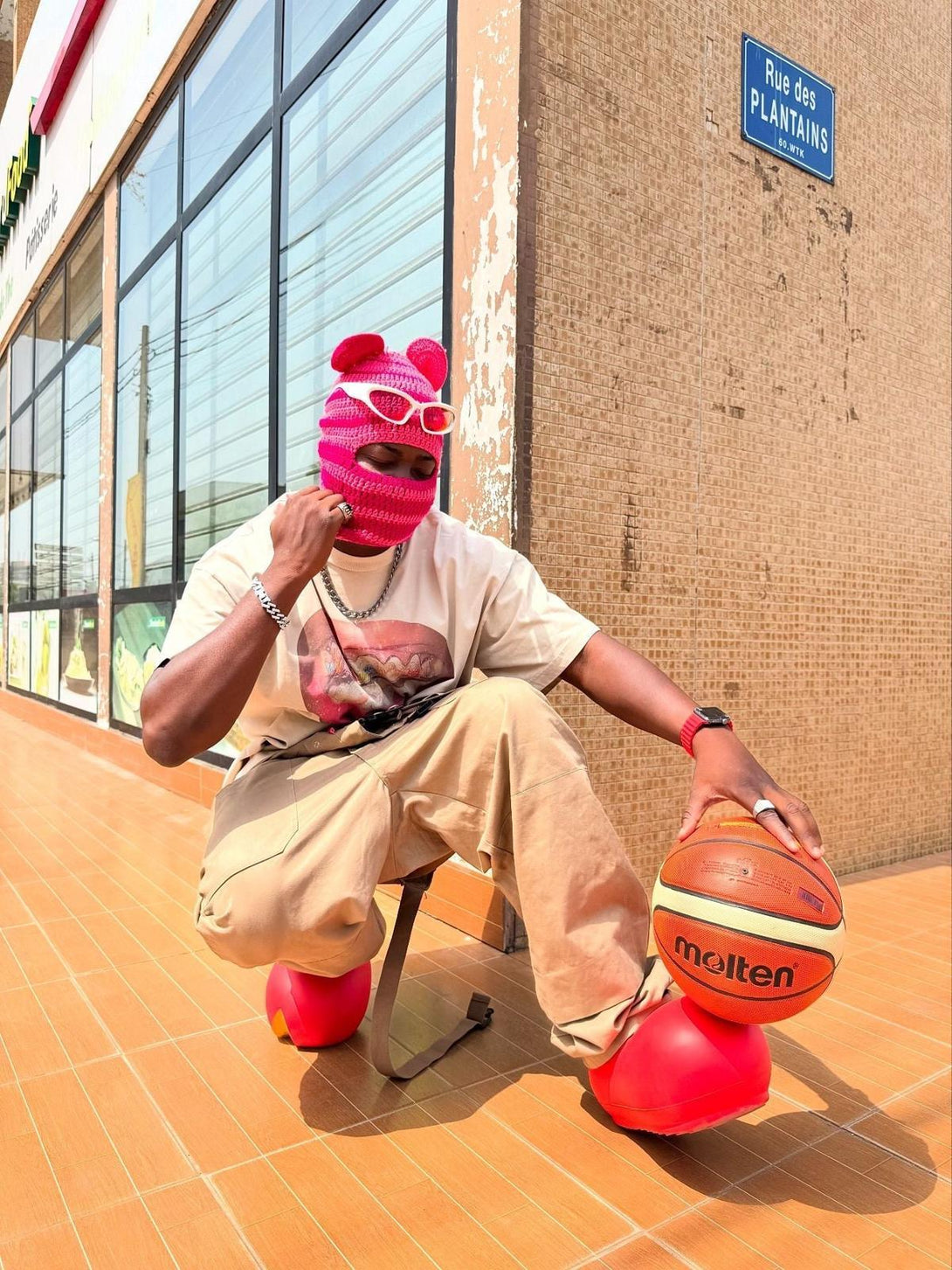 Model in a TALISHKO graphic tee and red accessories, posing with a basketball on a sunny street.