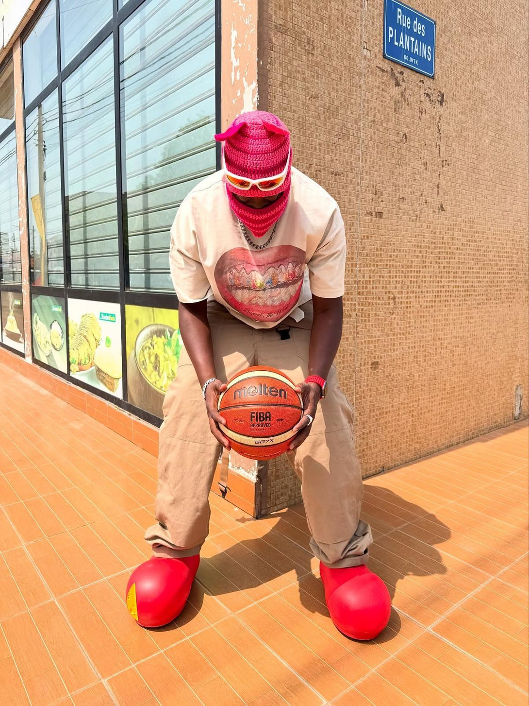Person in a TALISHKO graphic tee holding a basketball, styled with bold red accessories.
