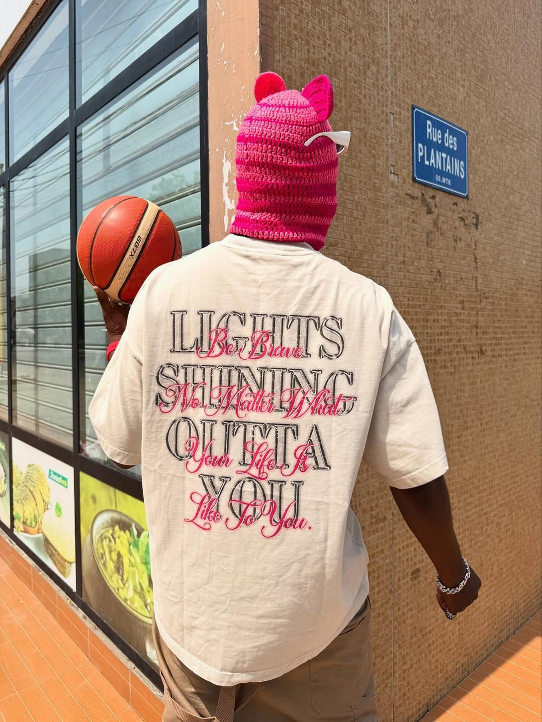 Person in a TALISHKO graphic tee with motivational print, styled with a pink knit hat and basketball.