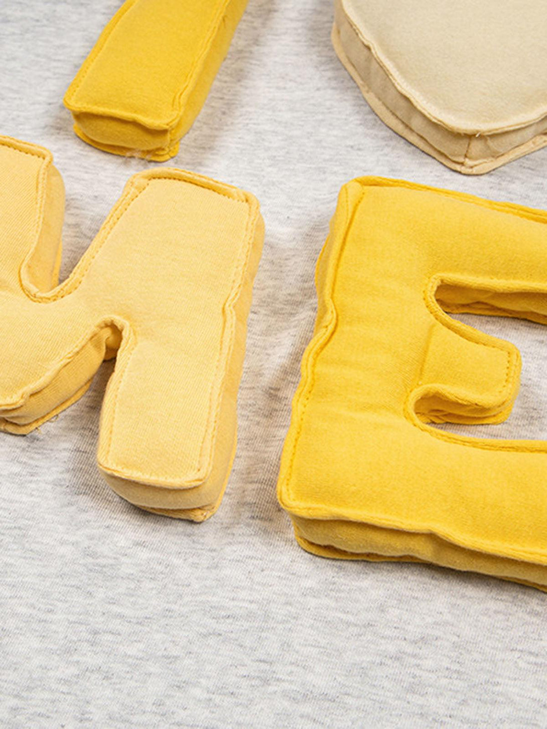 A detailed view of TALISHKO's yellow embroidered letters on a gray T-shirt, showcasing playful design.