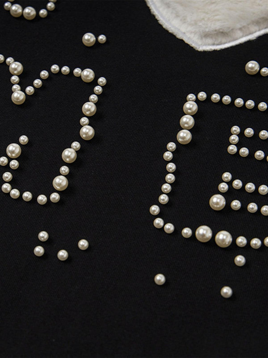Intricate look at pearl embellishments on a black T-shirt, highlighting TALISHKO's playful design.