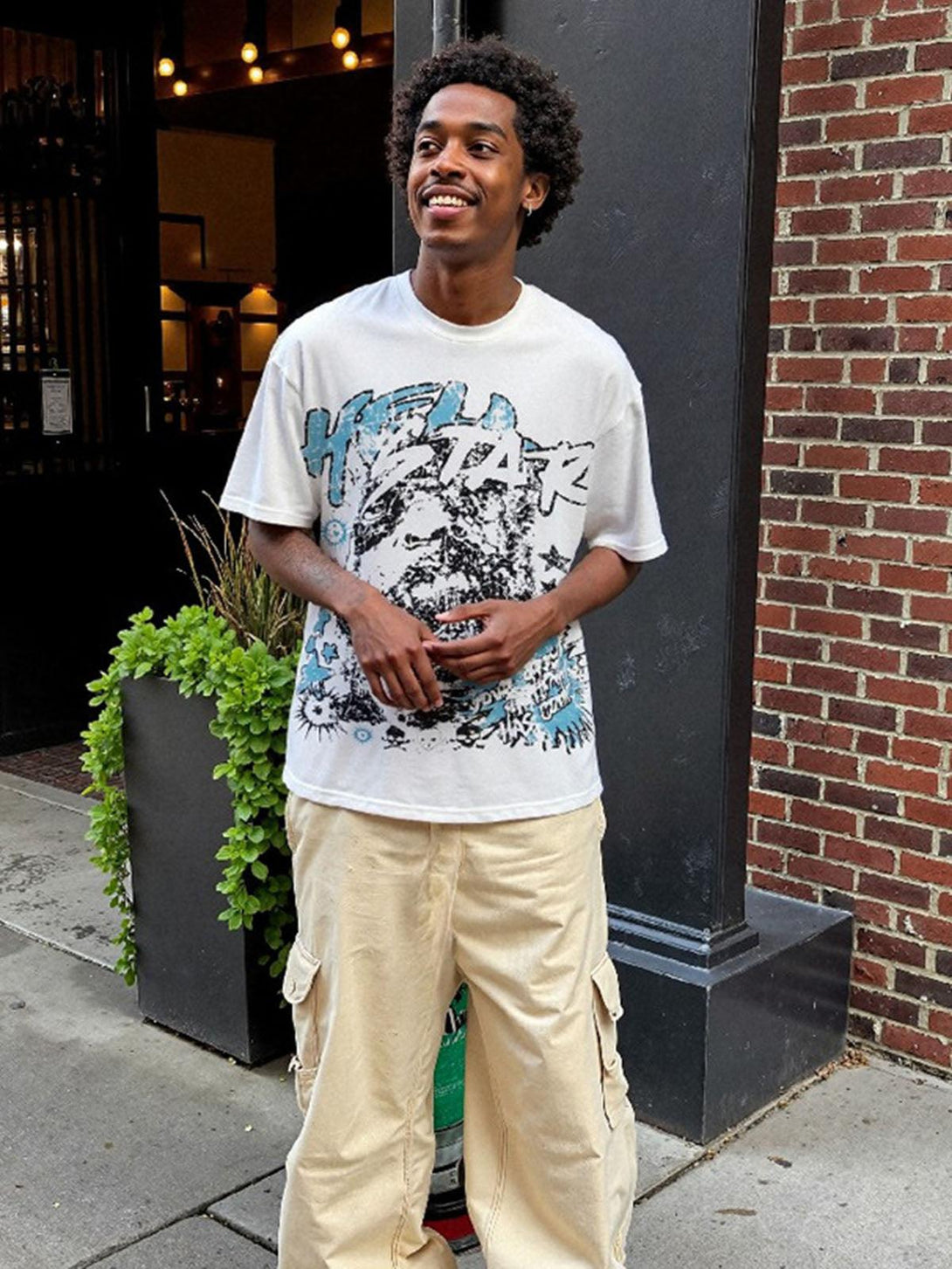 Model in a TALISHKO fun portrait graphic T-shirt paired with light cargo pants outdoors.