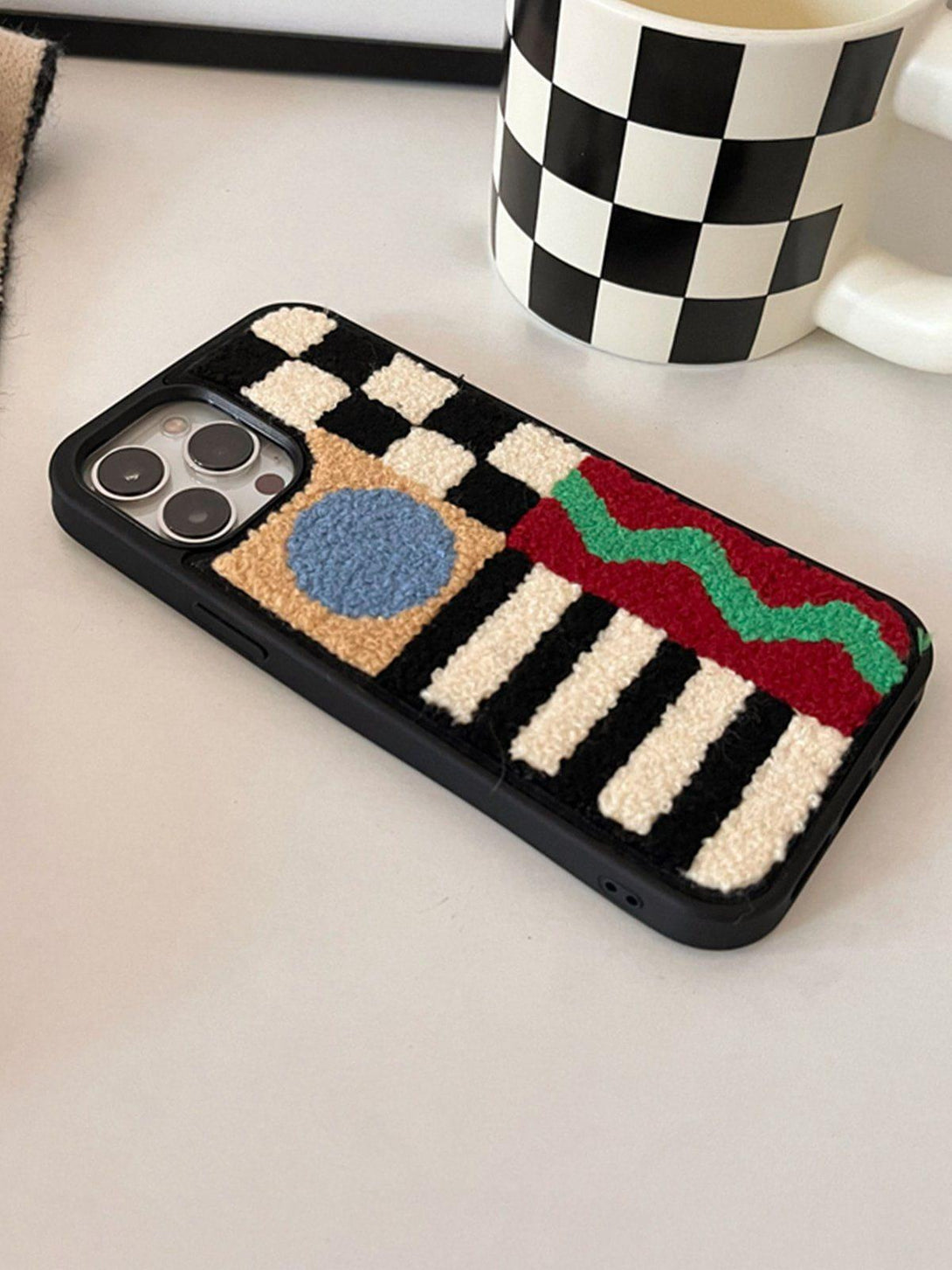 TALISHKO plush phone case features a geometric patchwork design with vibrant colors and textures.