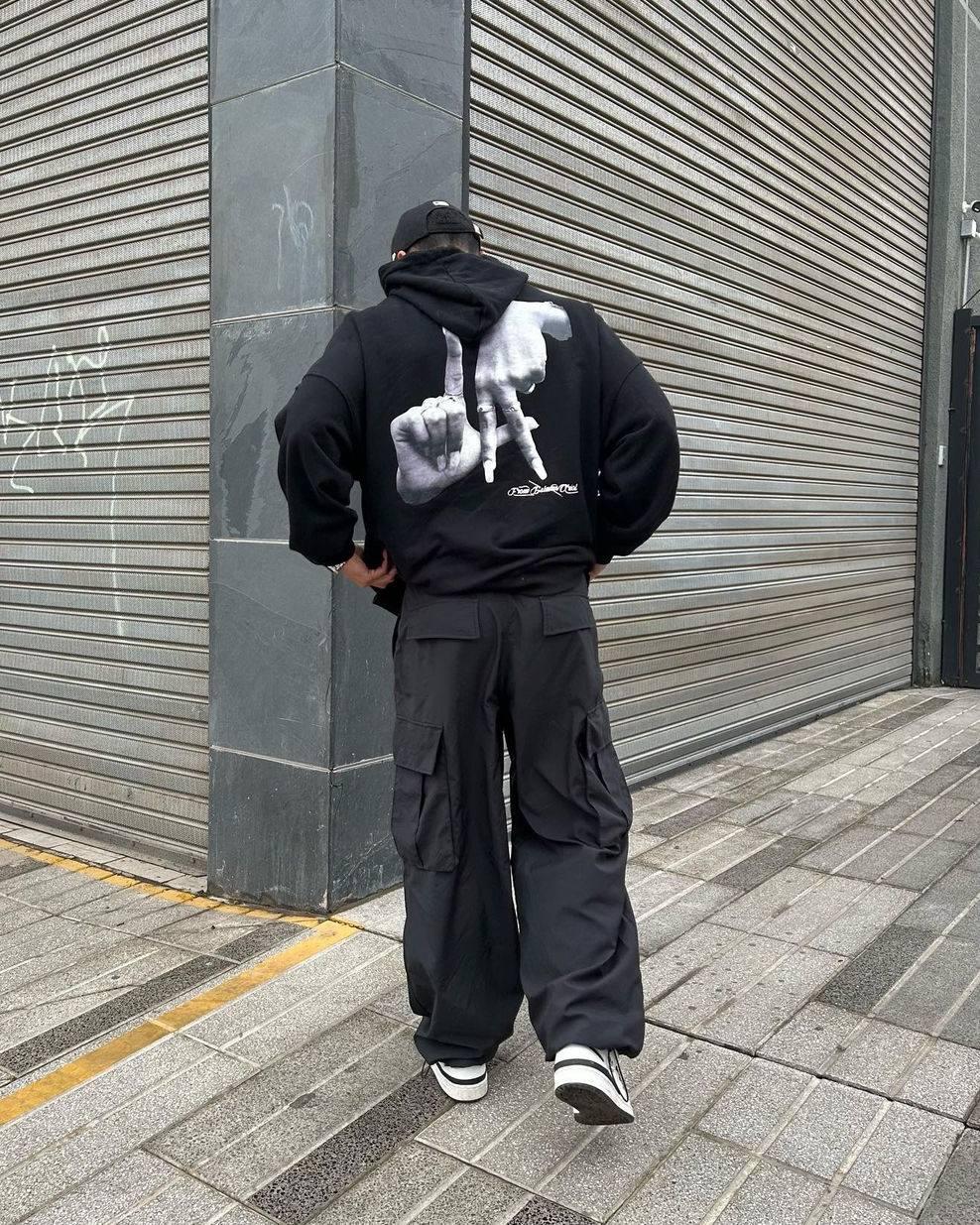 A man in a TALISHKO Gesture Print Hoodie with striking hand design, paired with cargo pants.