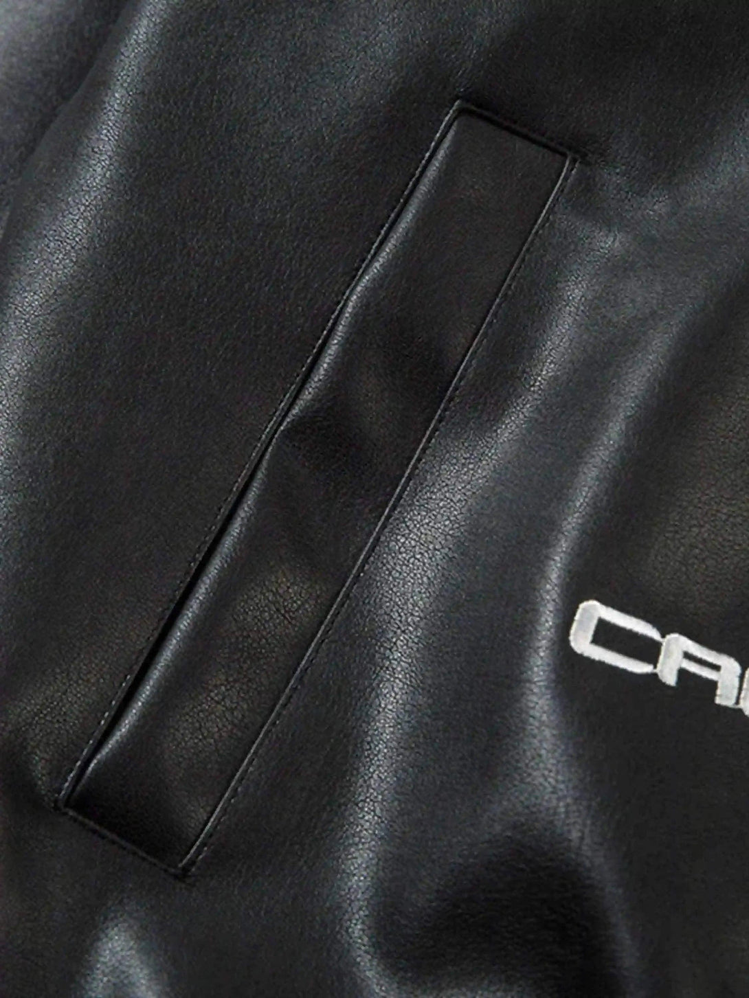 Detailed view of TALISHKO jacket's pocket design on sleek black fabric, highlighting texture.
