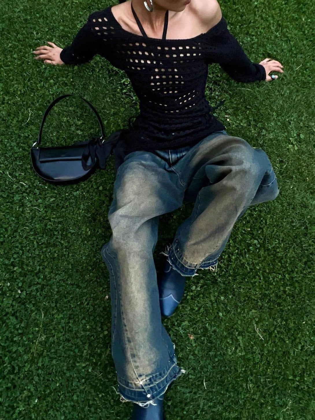 Model in TALISHKO gradient raw edge jeans and black knit top, relaxing on lush green grass.