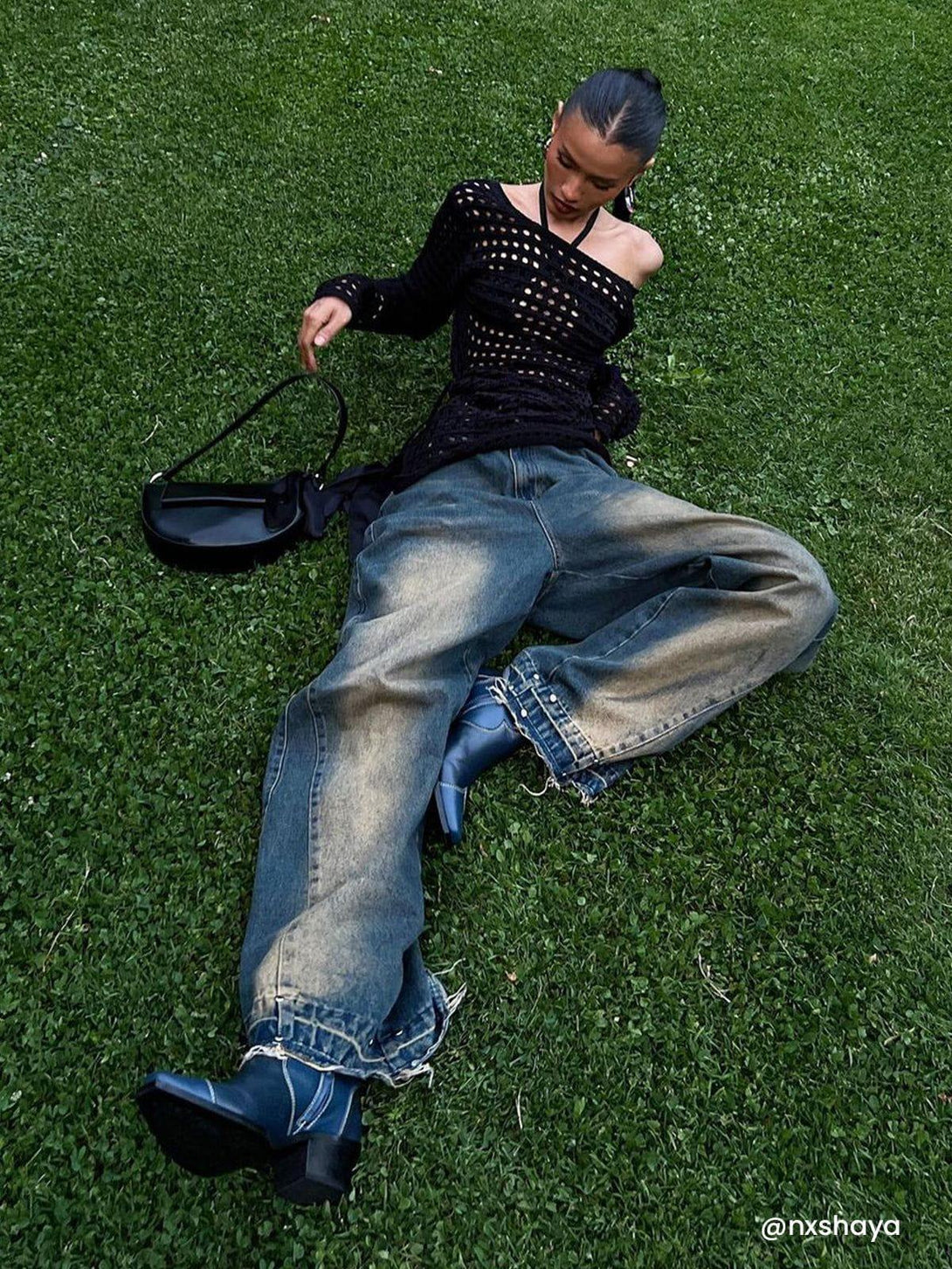 Model wearing TALISHKO’s gradient raw edge jeans with a black knit top, lounging on grass.
