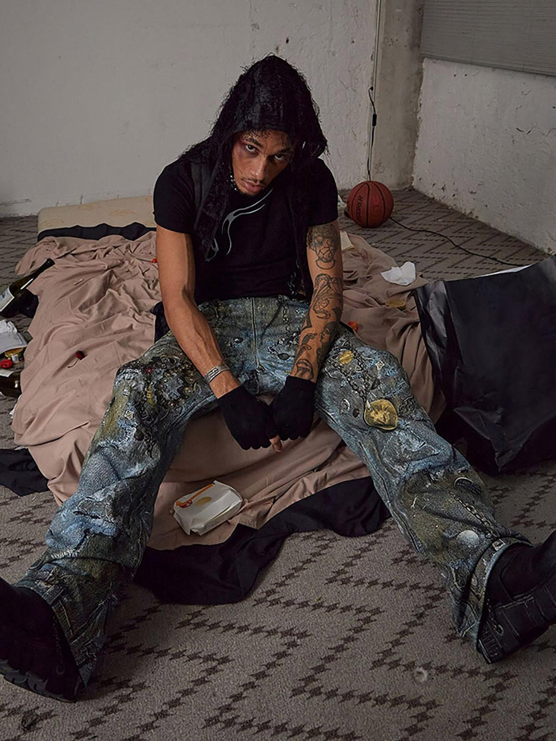 Model sitting in TALISHKO graffiti-inspired jeans, showcasing edgy style and detailed chains.