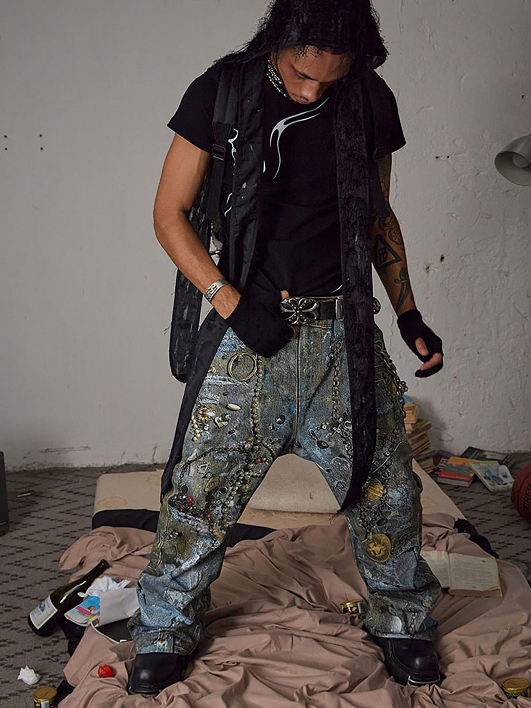Model in TALISHKO jeans with graffiti design and chains, paired with a black outfit in an urban setting.