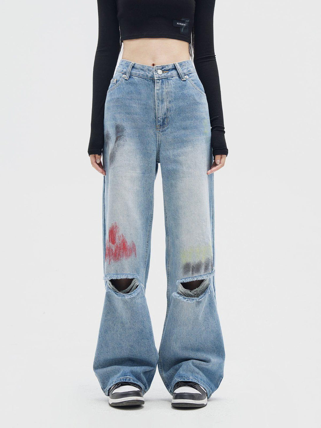 Model wearing graffiti distressed jeans by TALISHKO, featuring knee rips and artistic accents.