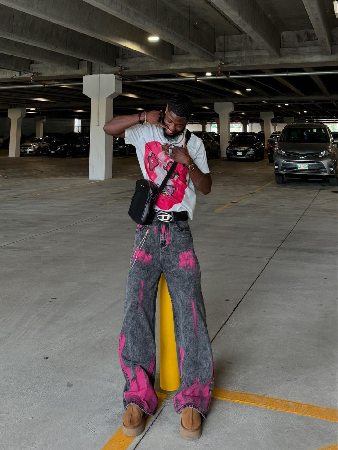 Model showcasing TALISHKO graffiti distressed baggy jeans with pink accents in a parking garage.