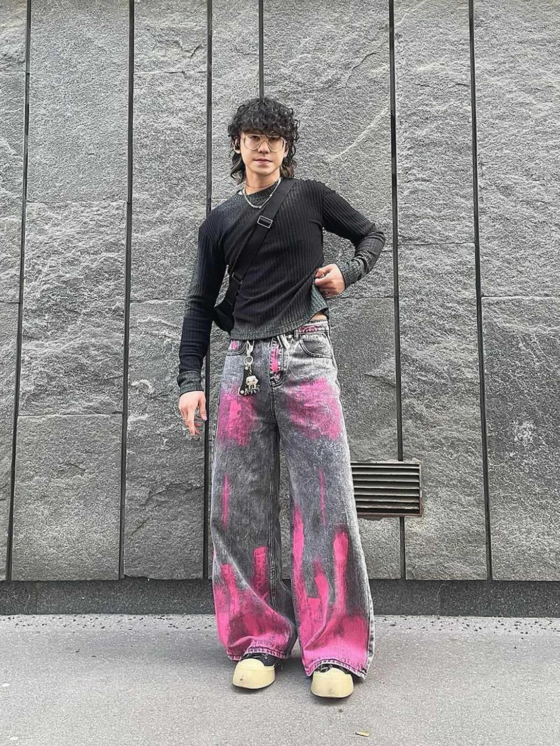 Model wearing TALISHKO graffiti-style baggy jeans with pink accents and black top in urban setting.