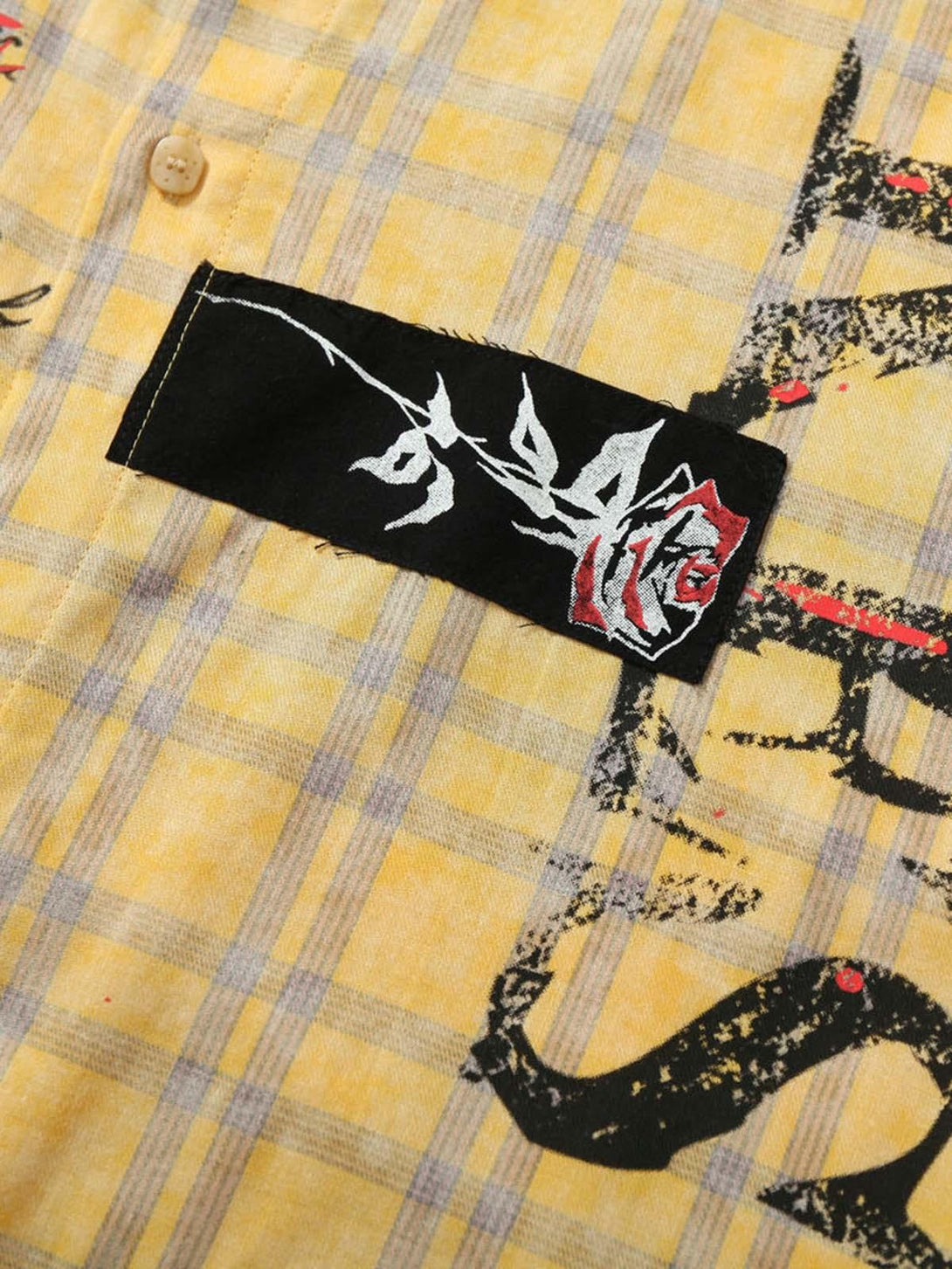 A detailed view of graffiti and rose embroidery on a yellow plaid shirt by TALISHKO.