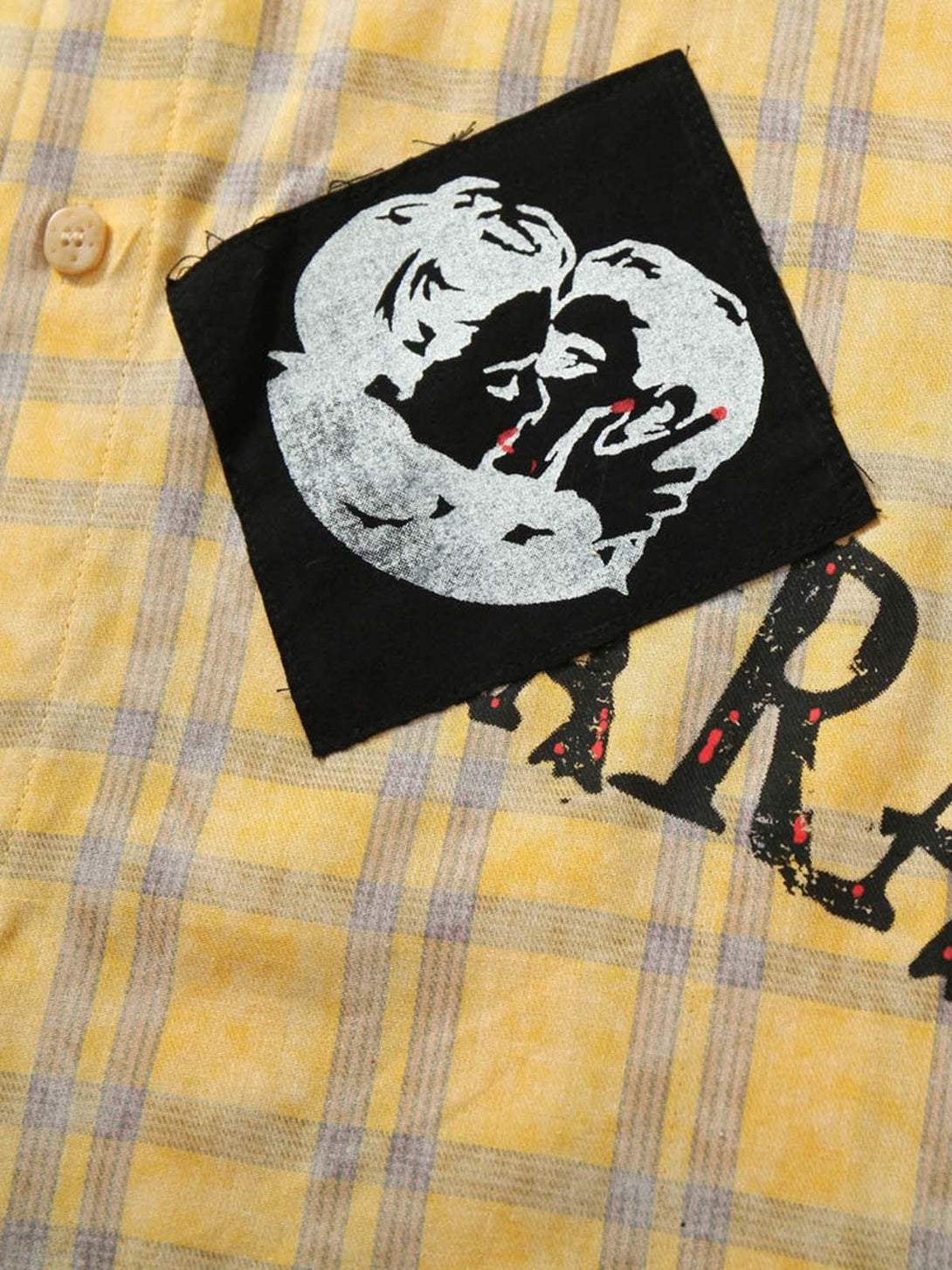 A close-up of TALISHKO's yellow plaid shirt, highlighting unique graphic patch details.