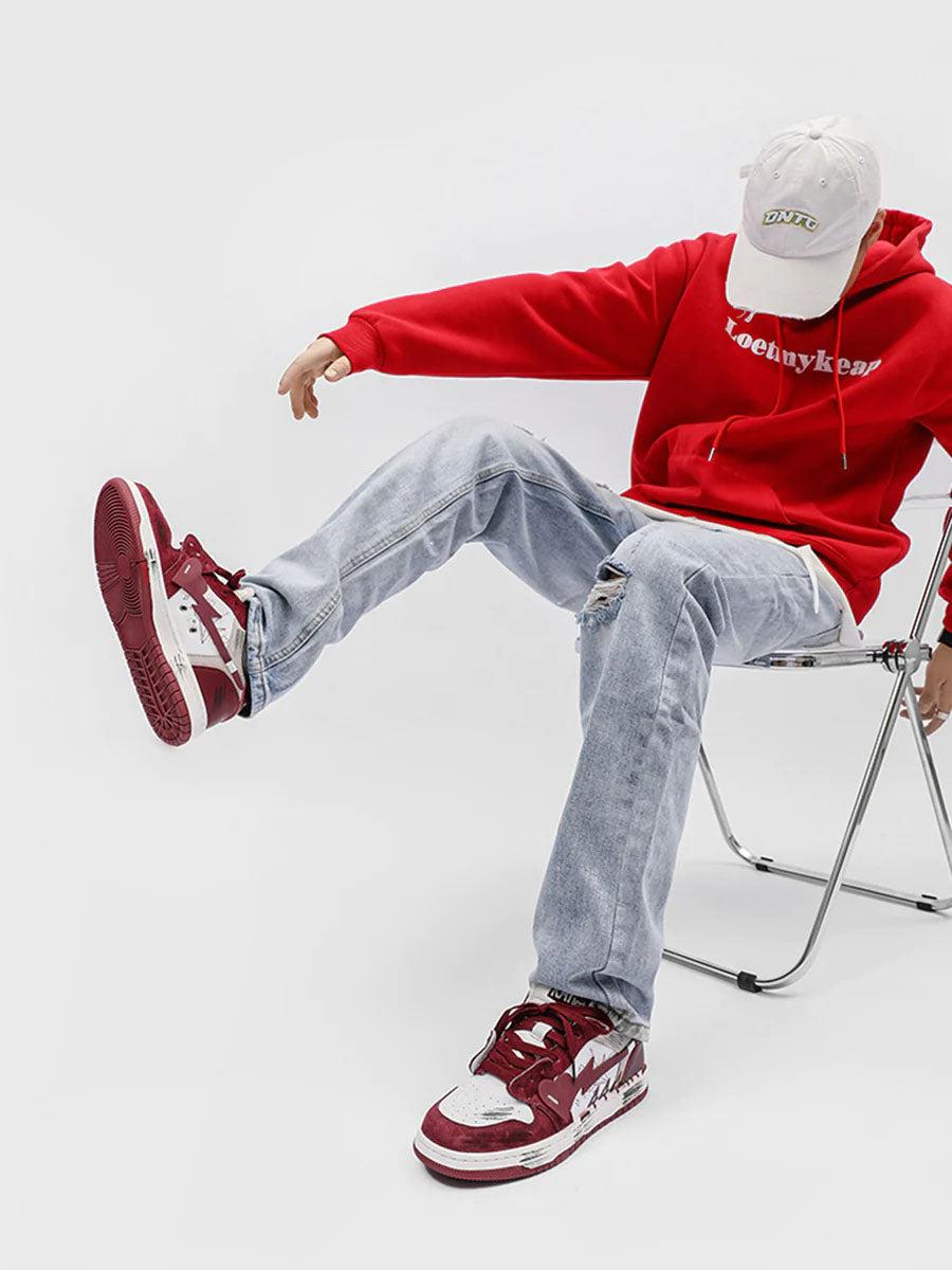 Model wearing TALISHKO graffiti skate shoes in red and white, paired with a red hoodie and jeans.
