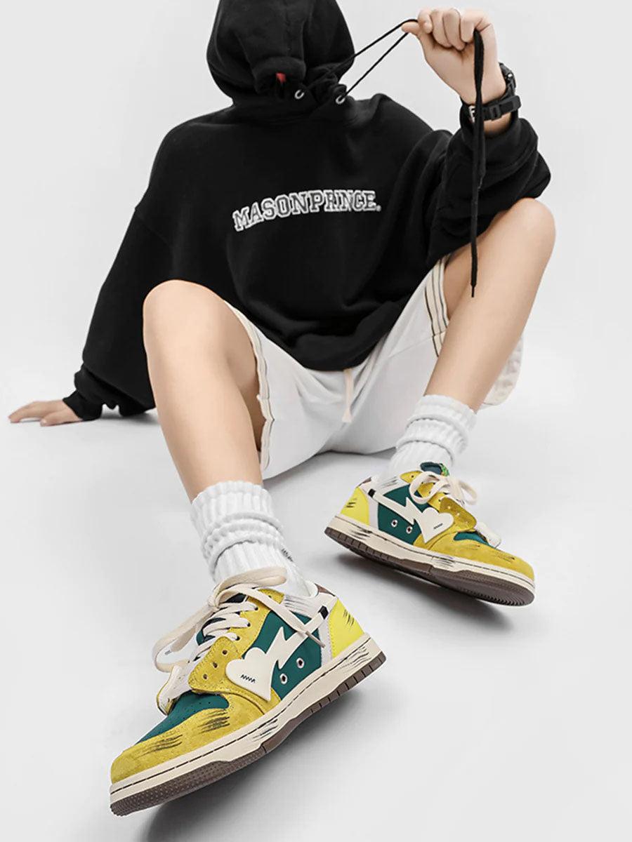 TALISHKO graffiti skate shoes in vibrant yellow and green, styled with a black hoodie and shorts.