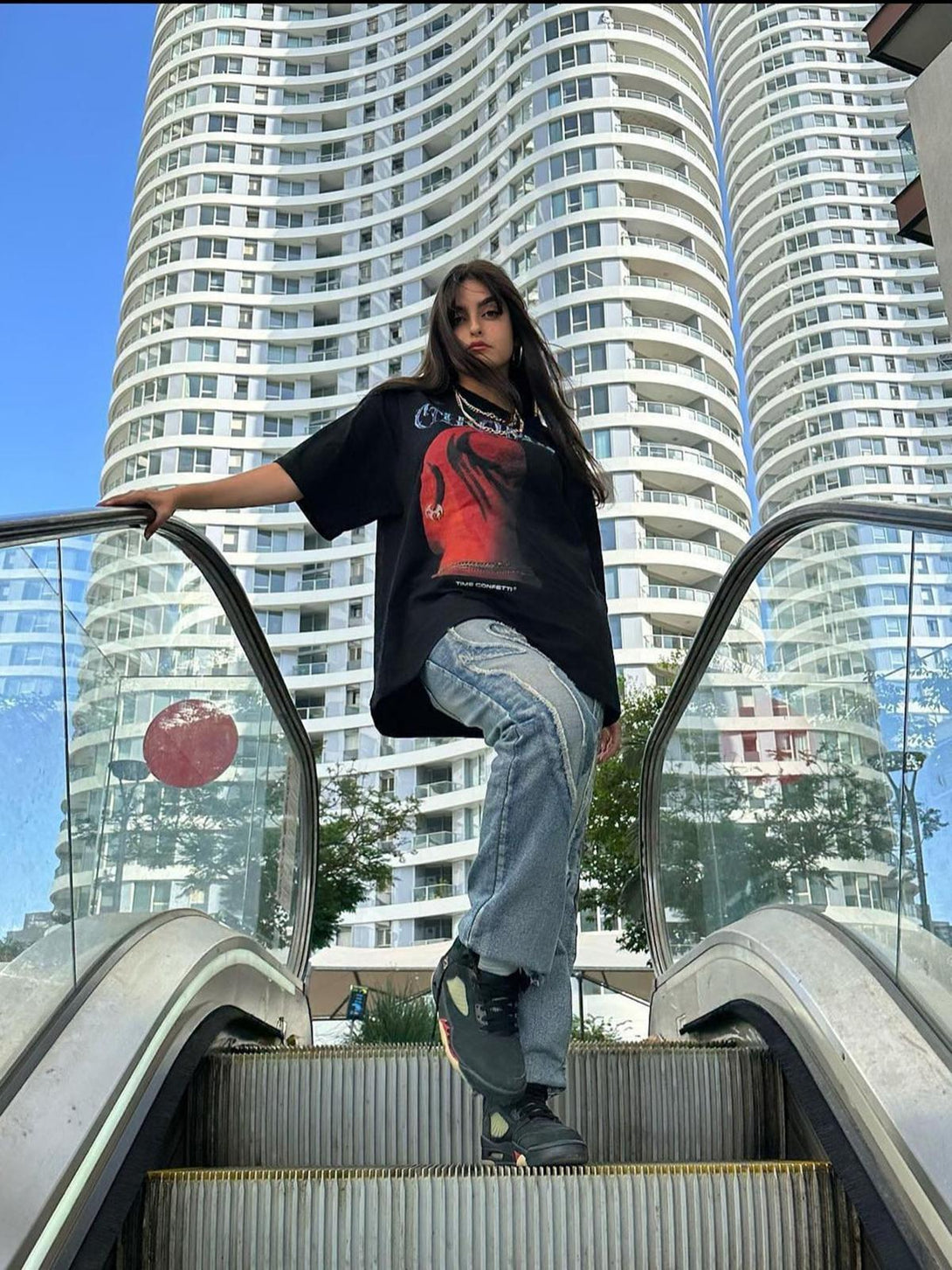Model on escalator wearing TALISHKO hip hop T-shirt with head print, blending urban street style.