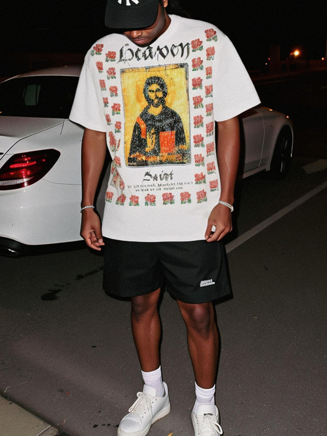 Model in TALISHKO T-shirt with floral and icon design, styled with black shorts and sneakers.