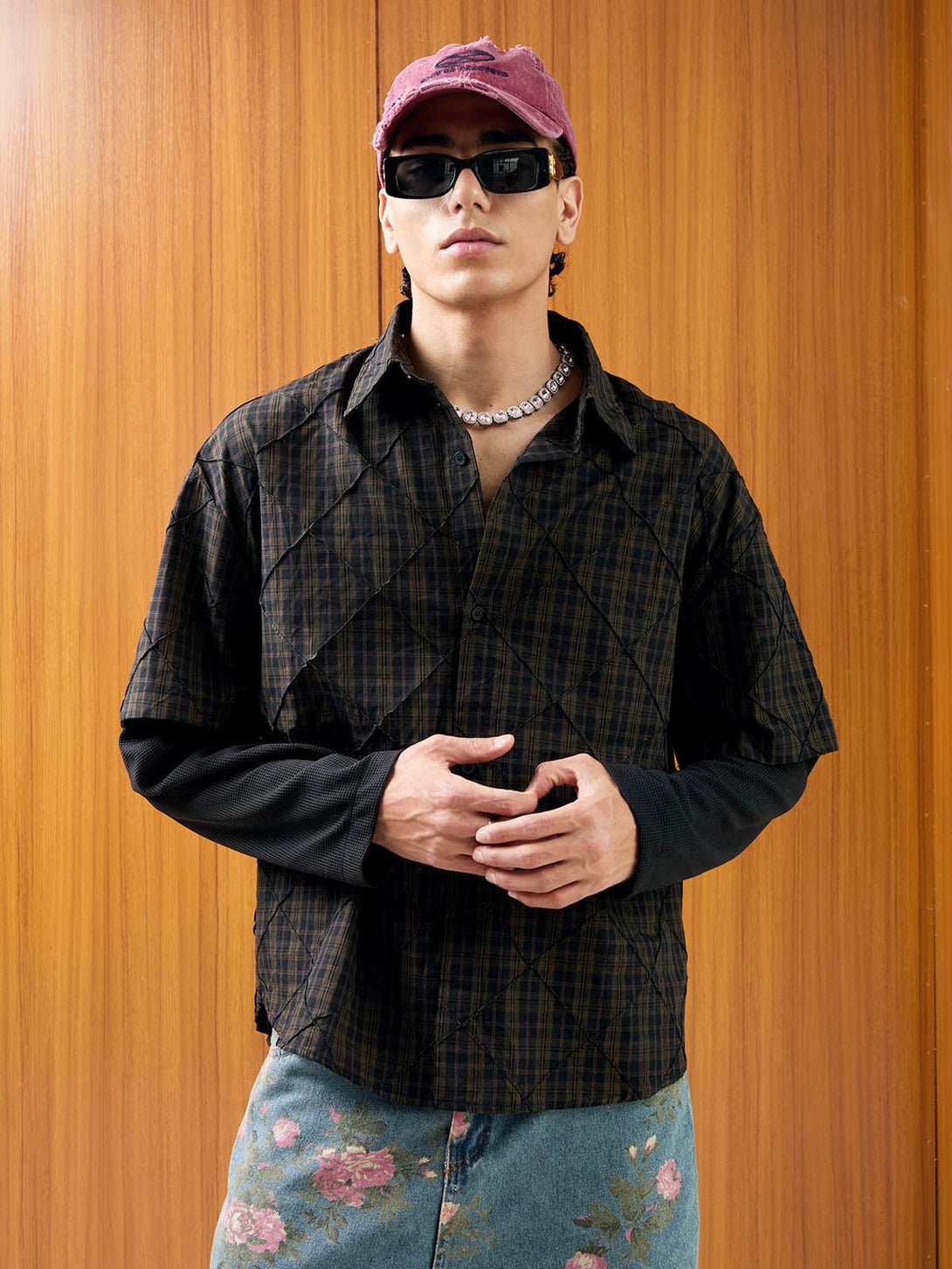 Model in a plaid polo shirt by TALISHKO, styled with floral denim and bold accessories.