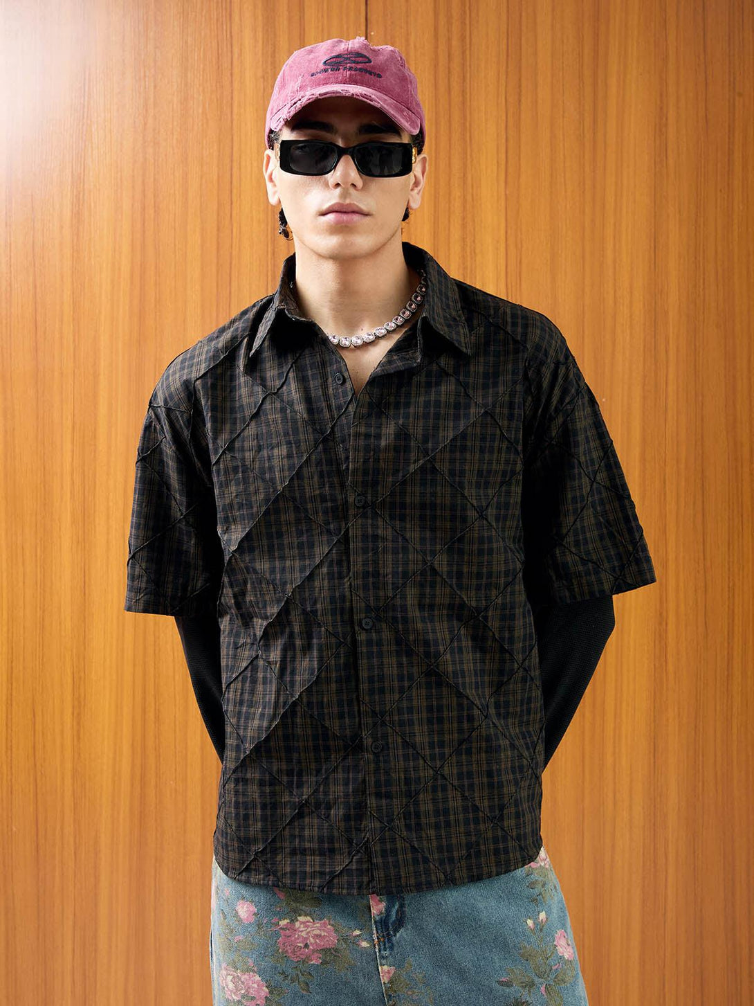 Model in a plaid pleated polo shirt by TALISHKO, styled with a pink cap and sunglasses.