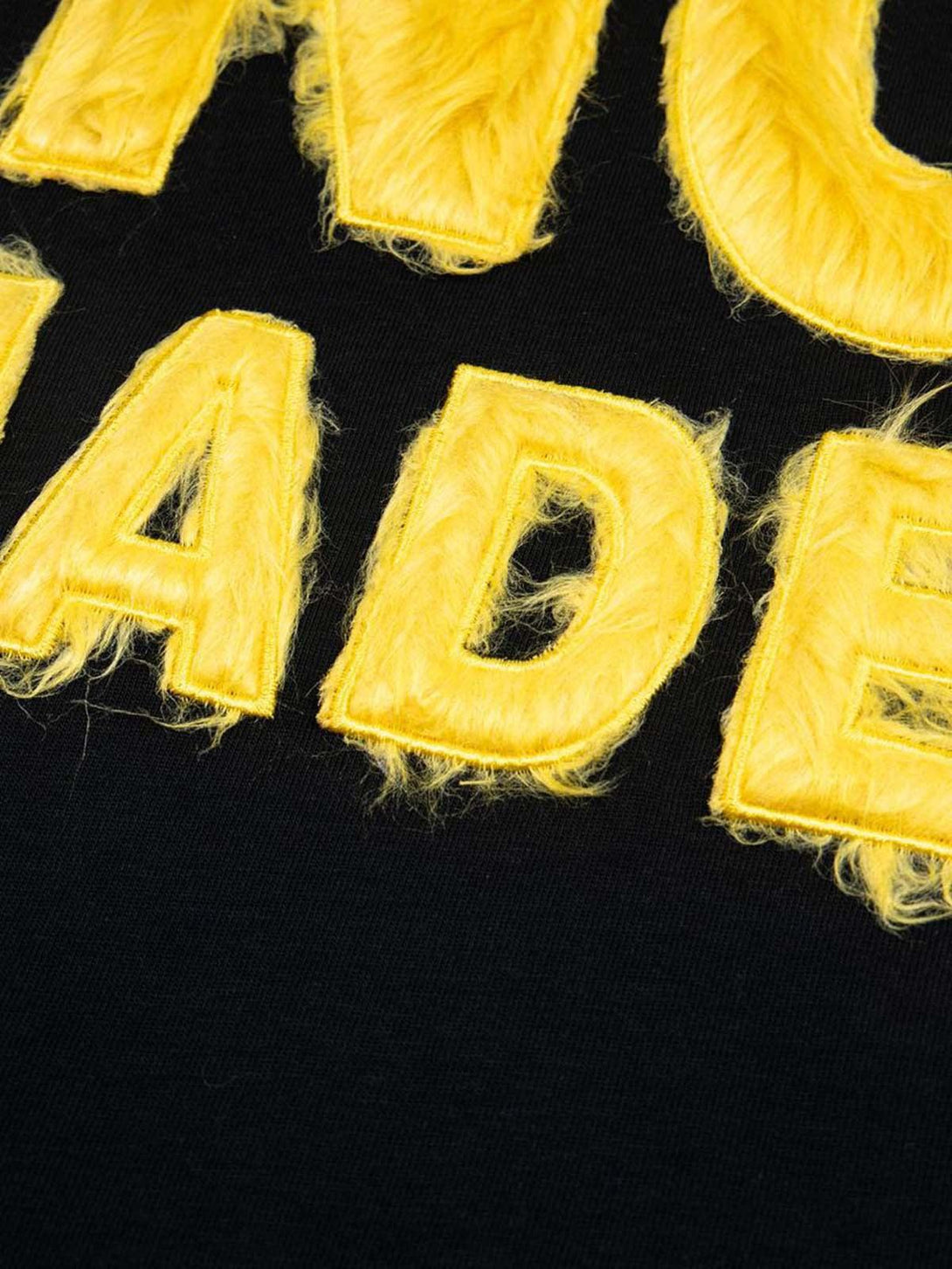 Fuzzy yellow lettering detail on a black TALISHKO T-shirt, showcasing retro-inspired texture.