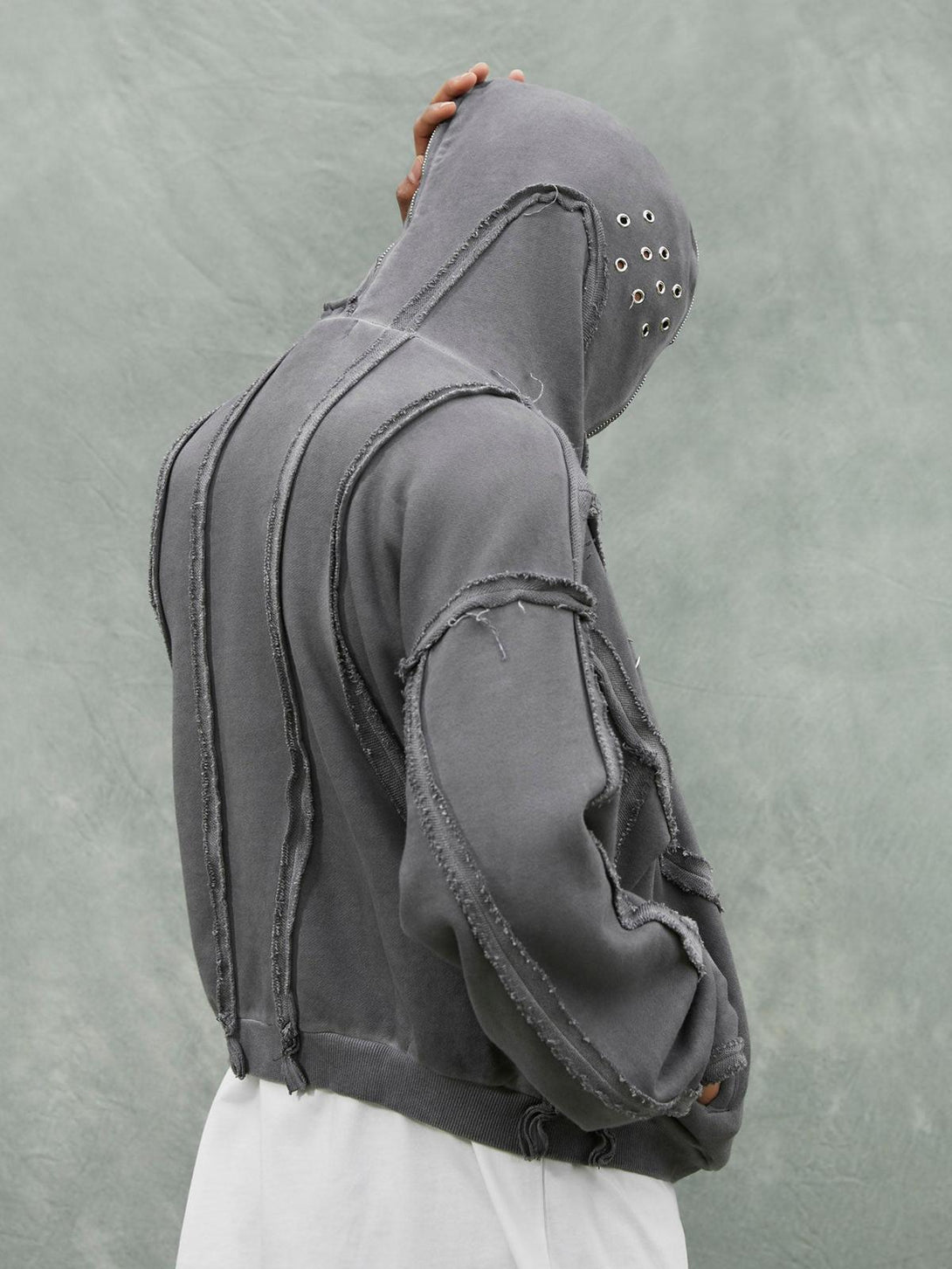 Side view of a TALISHKO distressed full zip hoodie, featuring raw edge seams and eyelet details.