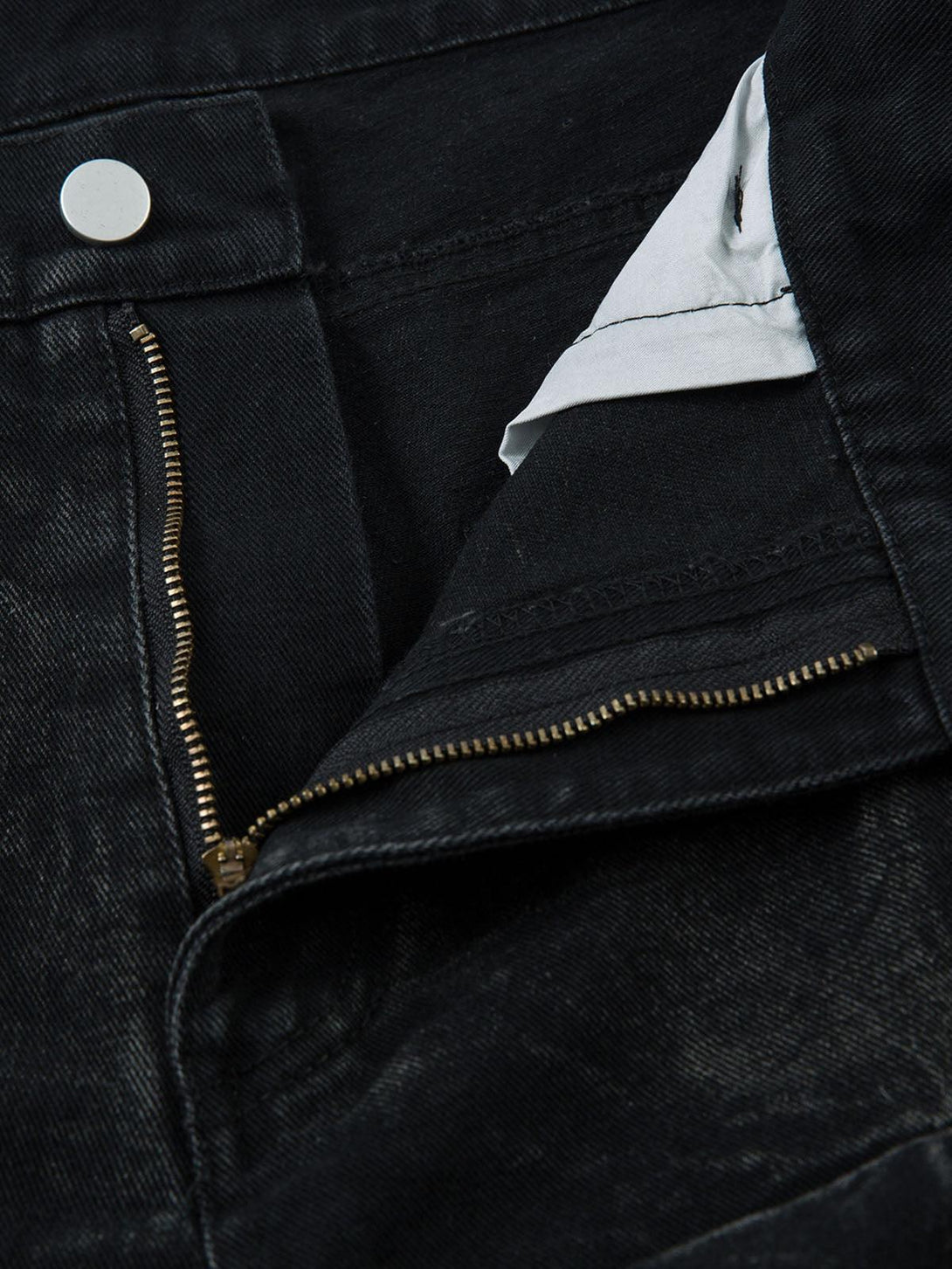 A detailed view of TALISHKO jeans featuring a gold zipper and distressed black fabric.