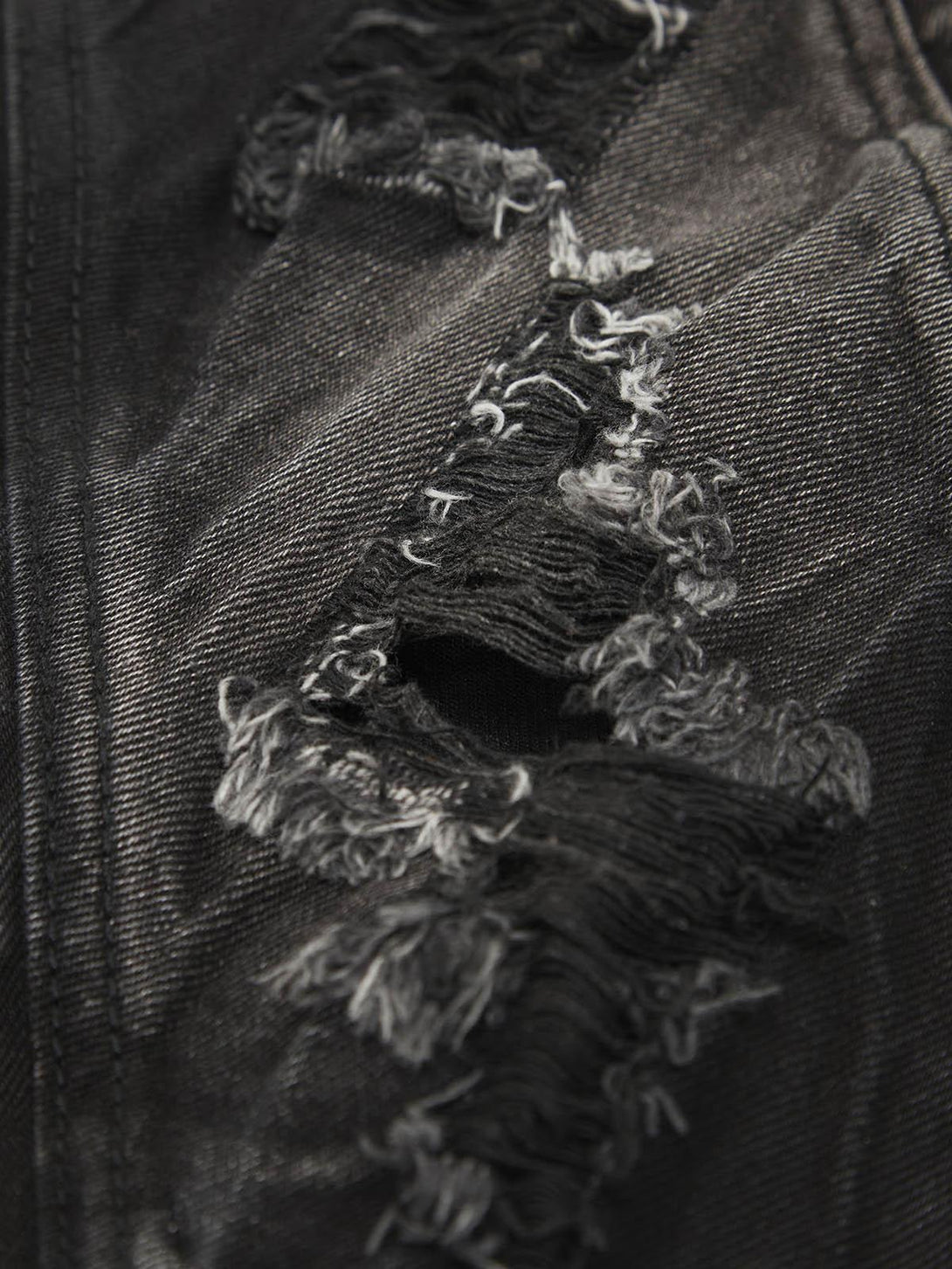 Zoomed-in texture of TALISHKO jeans showcasing the ripped details and rugged black fabric.