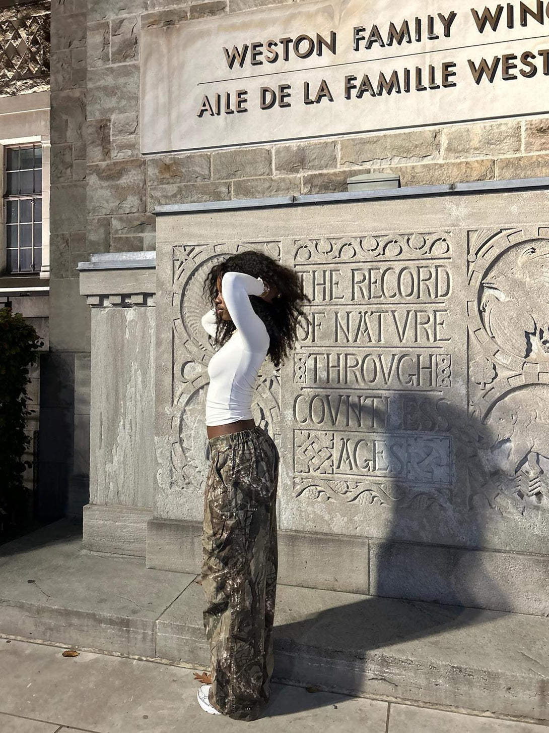 Side view of TALISHKO camouflage pants paired with a white top, highlighting casual style.