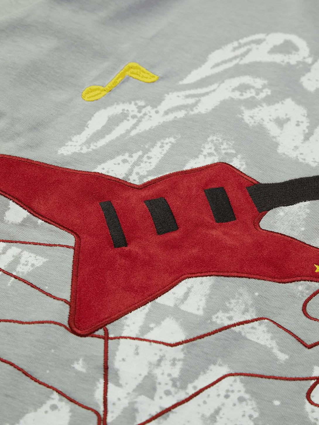 Zoomed-in detail of TALISHKO's T-shirt, showcasing a vibrant red guitar and musical note embroidery.