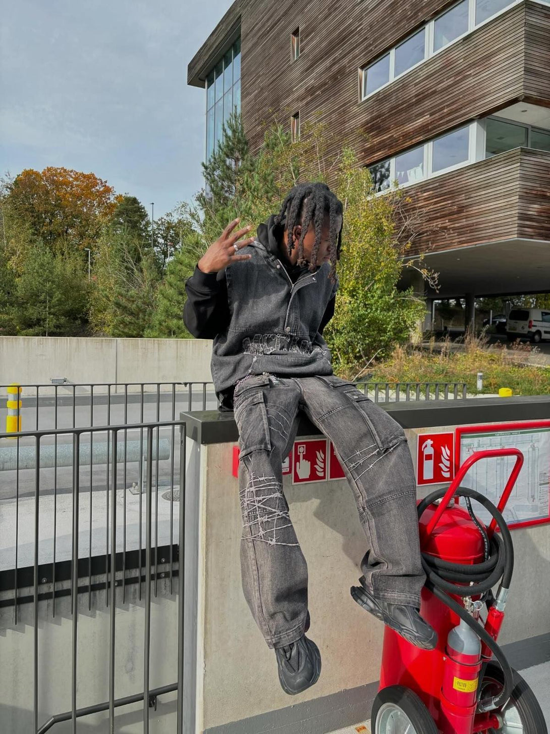 Model sitting outdoors in TALISHKO hip-hop jeans, featuring edgy barbed wire embroidery.