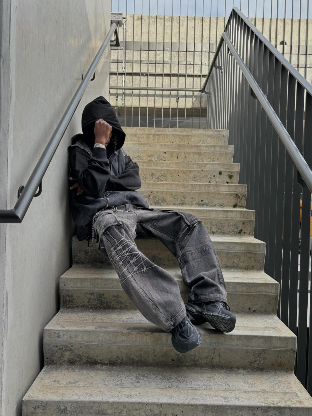 Model resting on stairs in TALISHKO hip-hop jeans, showcasing unique barbed wire embroidery.