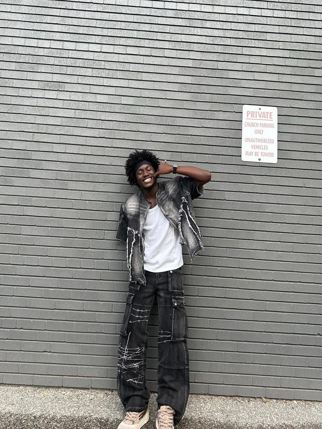 Model wearing TALISHKO hip-hop jeans with edgy barbed wire embroidery against a brick wall.