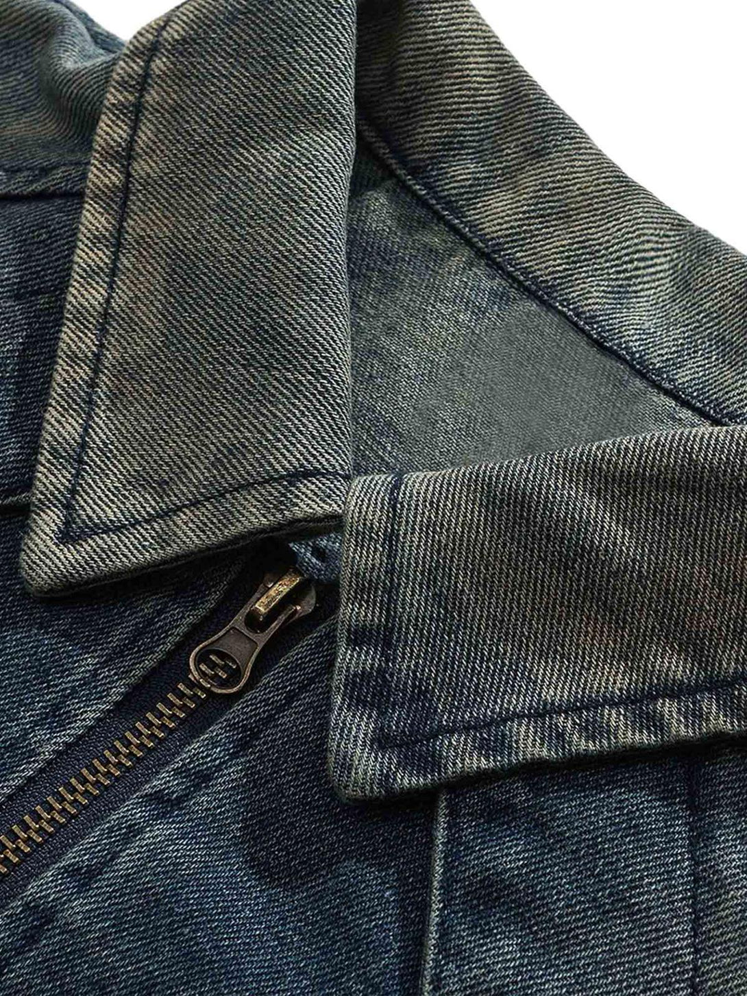 A close-up of the distressed denim jacket's collar and zipper by TALISHKO, highlighting texture.