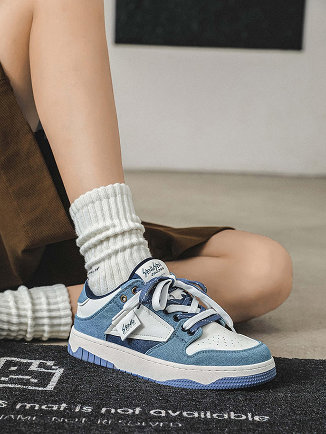 Model sitting with TALISHKO blue and white sneakers, featuring a casual and trendy style.