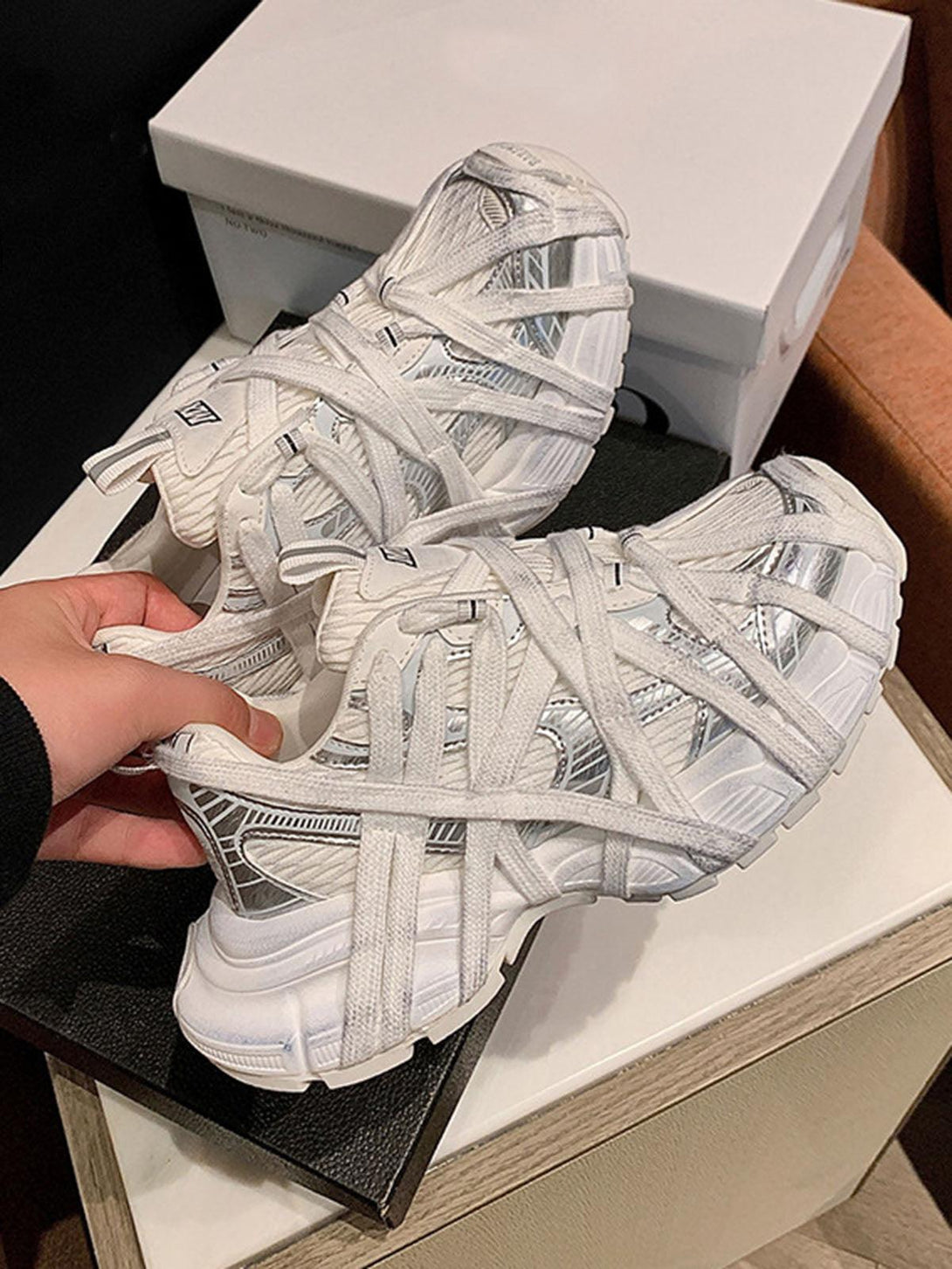 Hand holding white lace-up sneakers by TALISHKO, showcasing intricate design and urban style.