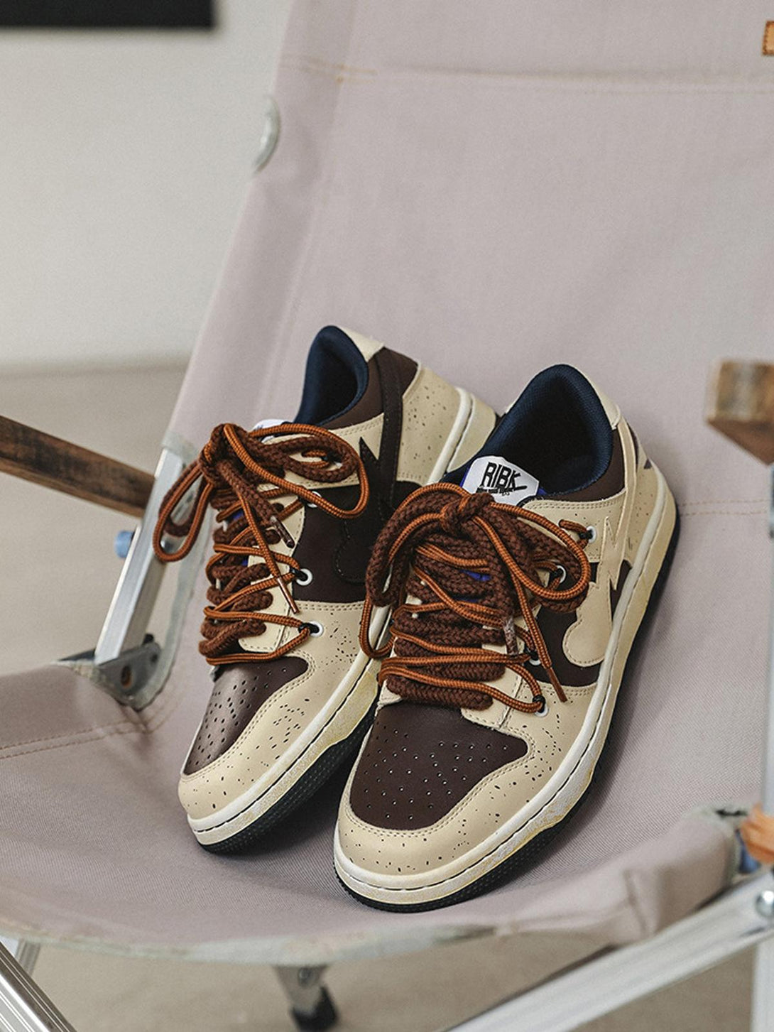 TALISHKO sneakers in brown and cream with contrasting laces, casually placed on a chair.