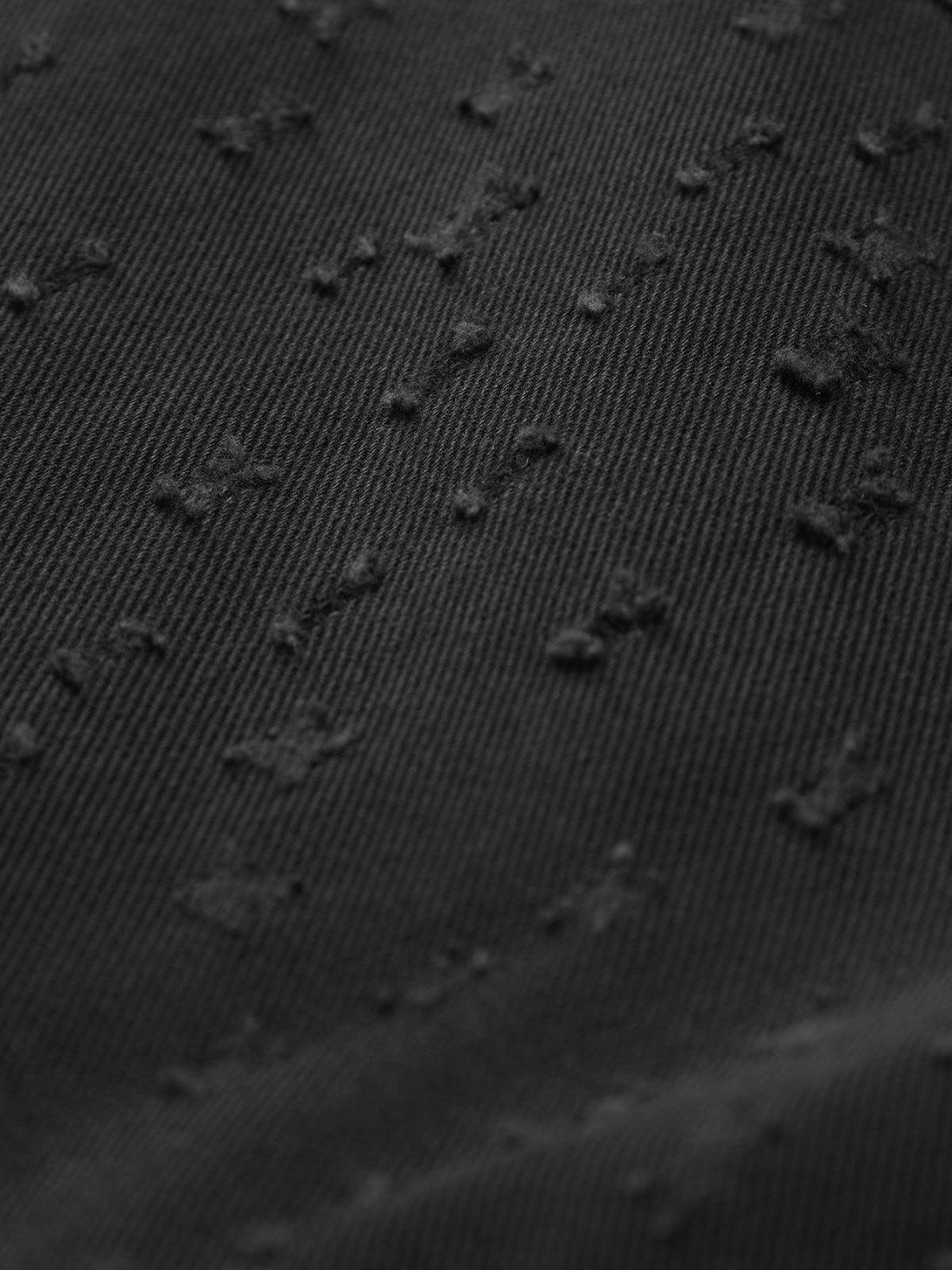 Zoomed-in texture of black denim shorts by TALISHKO, showcasing intricate design details.
