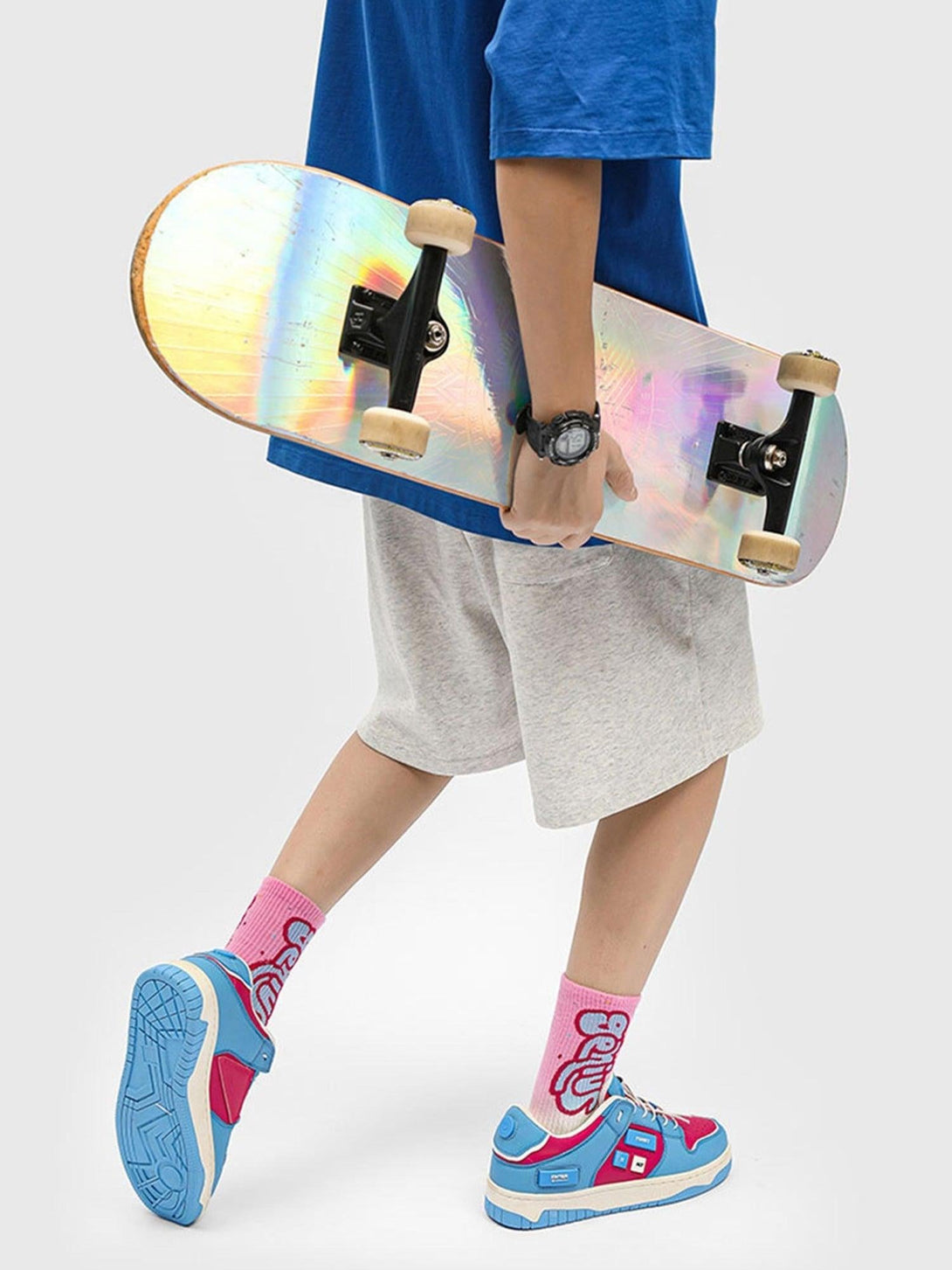 Person holding a skateboard and wearing TALISHKO skate shoes with vibrant blue and pink design.
