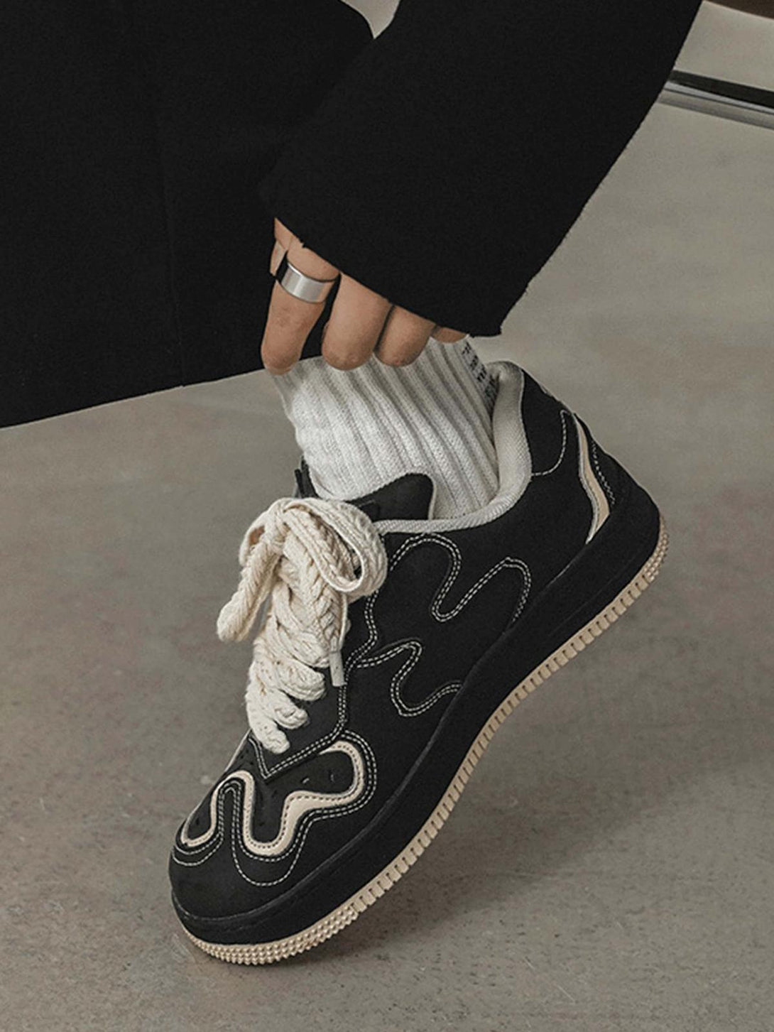 A close-up of TALISHKO skateboard shoes in black, highlighting bold cream laces and design.