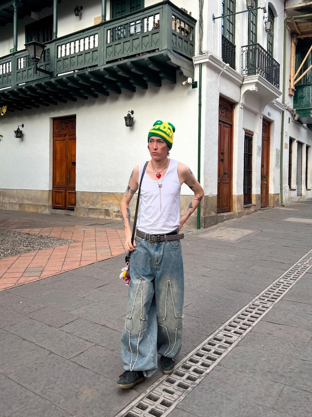 Model in TALISHKO washed jeans, styled with a tank top and vibrant beanie on a city street.