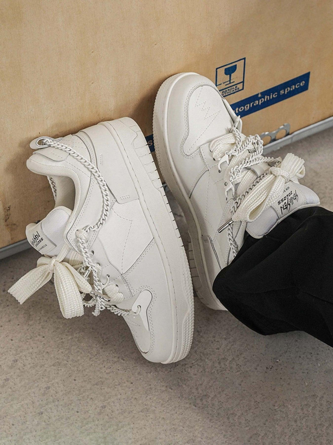 White TALISHKO sneakers with chain accents, styled with black pants for a modern street vibe.