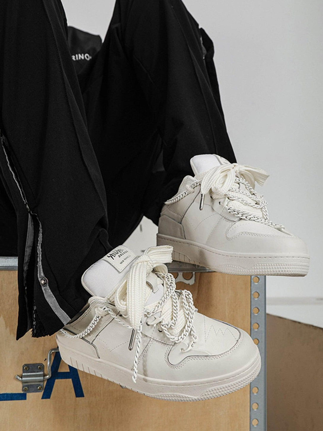 Model wearing TALISHKO white sneakers with chain details, styled with black pants for a trendy look.