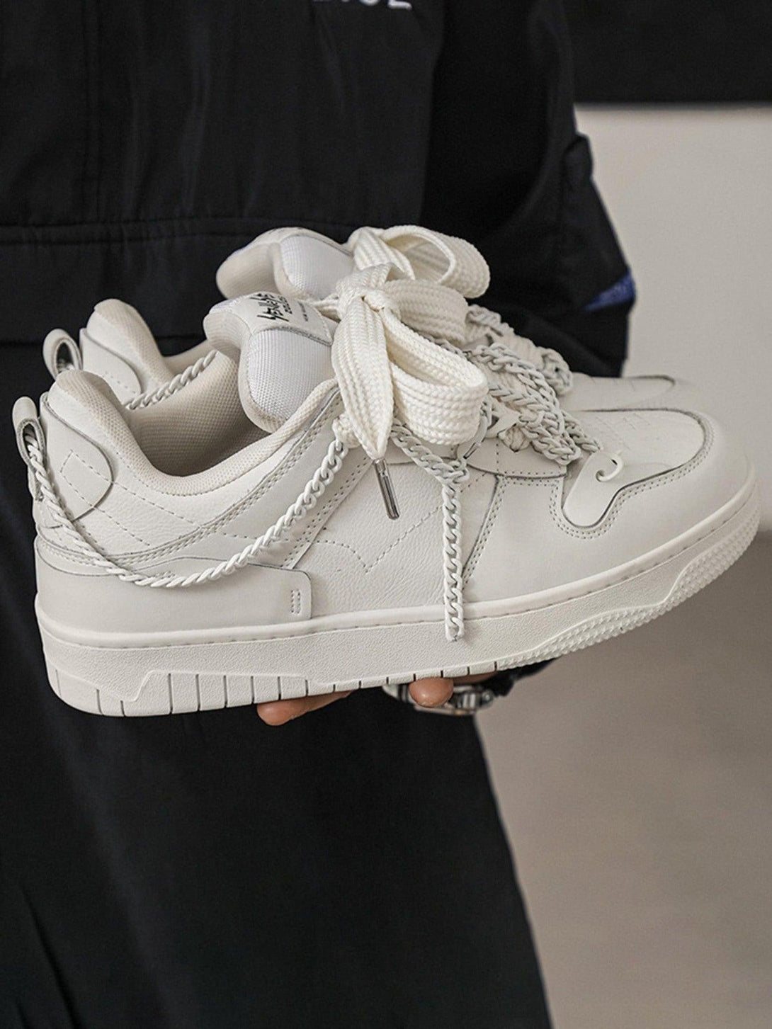 Stylish TALISHKO sneakers in white, featuring chain details, held casually for a chic look.
