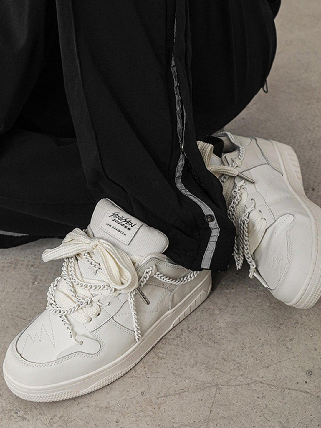 White TALISHKO board shoes with chain details, paired with black pants for a sleek urban look.